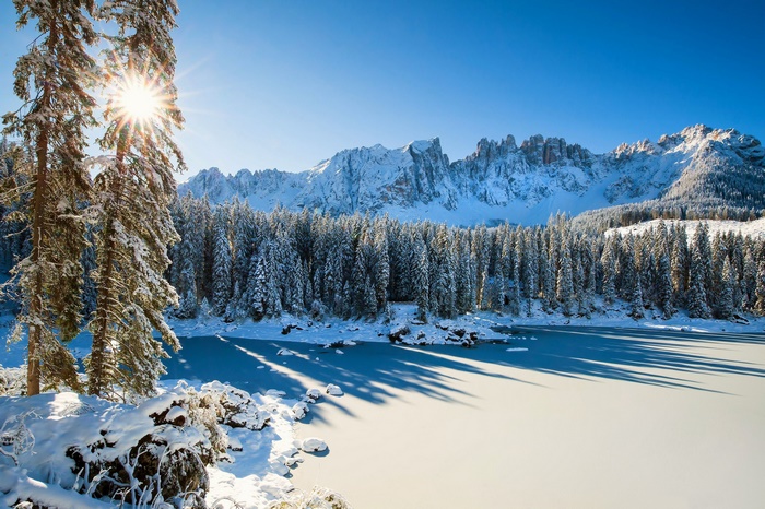 Frozen lake with snow-covered trees and mountains in the Dolomites, Italy
