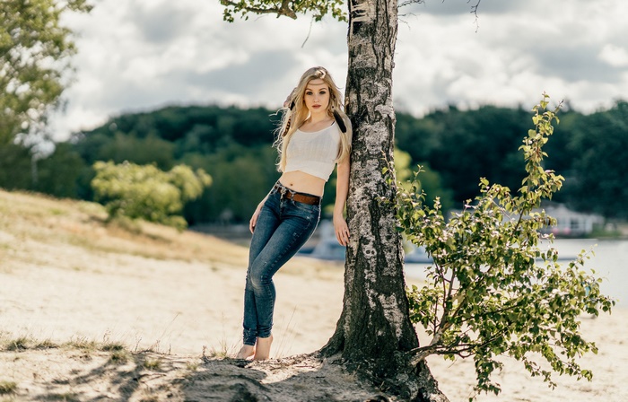 Blonde model in jeans leaning against a tree