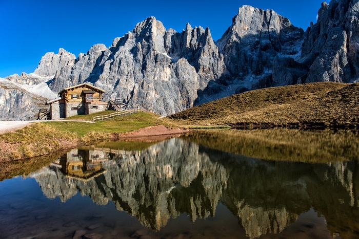 Log cabin by a mountain lake with Dolomites reflection