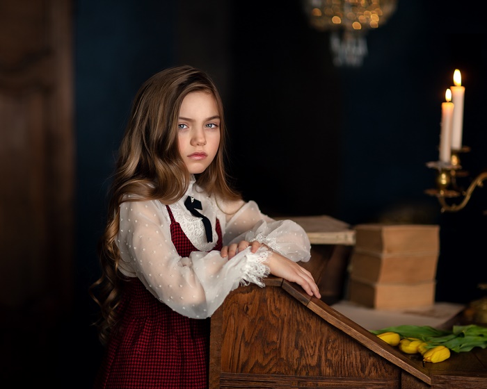 Girl with long hair by a wooden desk with books and candles