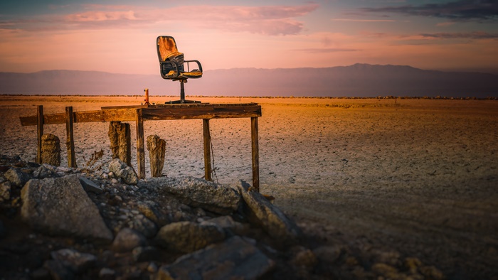 Office chair on a wooden platform in a desert at sunset