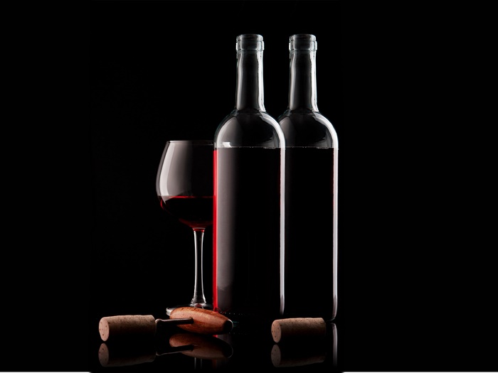 Two bottles of red wine, a glass, and a corkscrew
