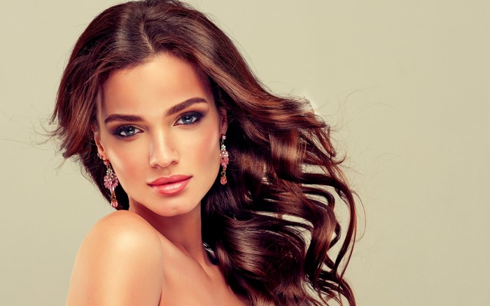 Woman with brown wavy hair and pink earrings