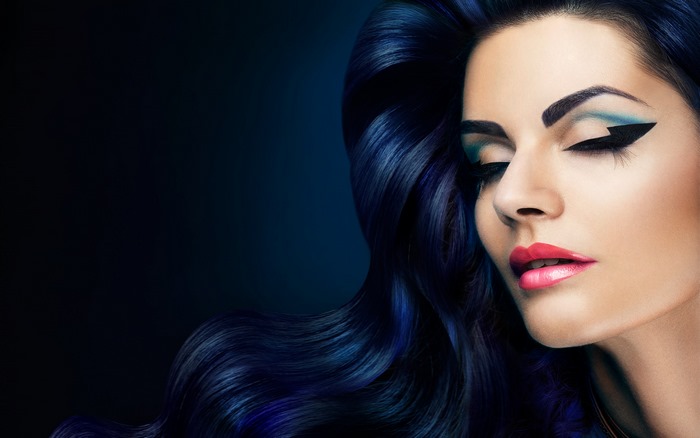 Woman with dark blue wavy hair and dramatic makeup