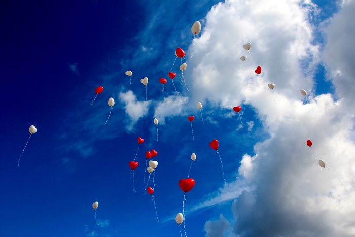 Red and white heart balloons in a cloudy blue sky