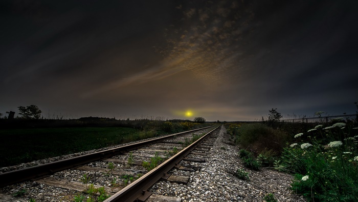 Railroad tracks stretching towards the horizon under a cloudy sky