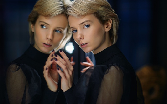 Woman with blonde short hair and blue eyes reflected in a mirror