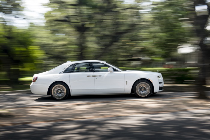 White Rolls-Royce Ghost driving on a tree-lined street