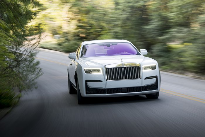 White Rolls-Royce Ghost driving on a tree-lined road