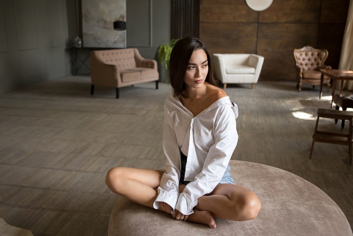 Brunette model in white shirt and shorts sitting on ottoman