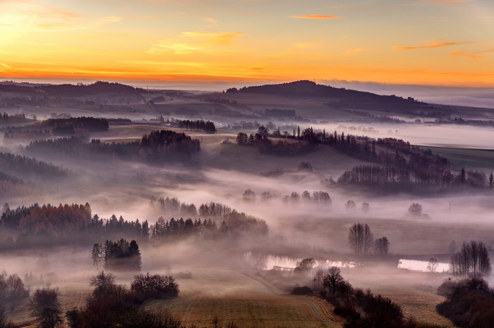 Misty valley landscape at sunrise with orange sky