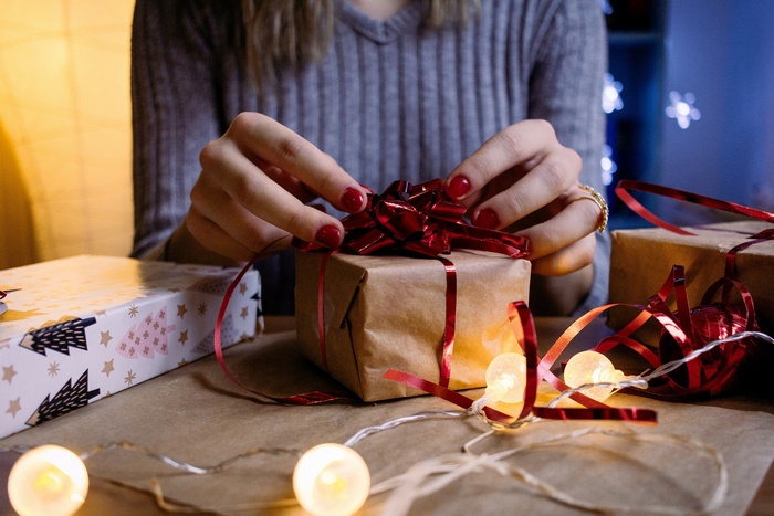 Hands wrapping a Christmas gift with red ribbon
