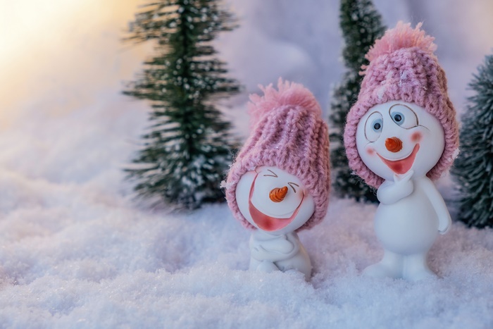 Two snowmen figurines in pink hats in the snow