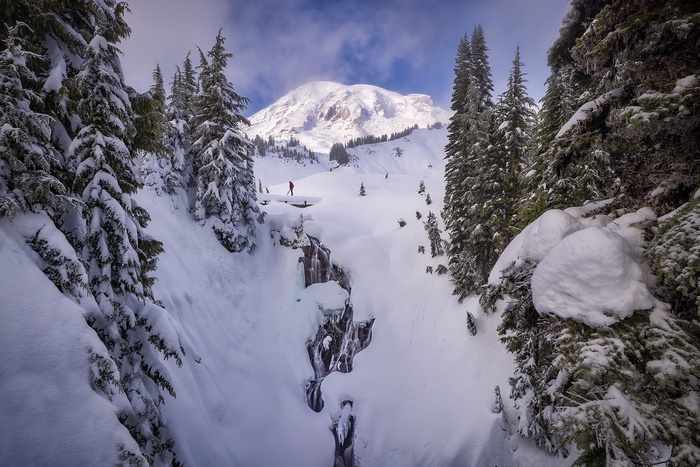 Man standing by frozen waterfall with Mount Rainier in background