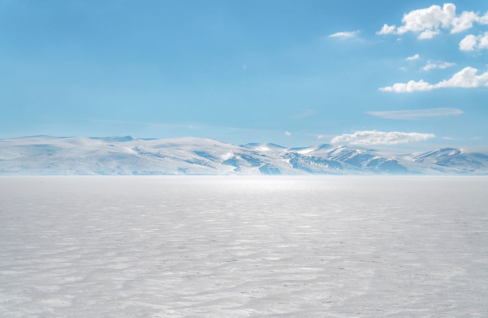 Snowy mountains over a frozen lake under a blue sky