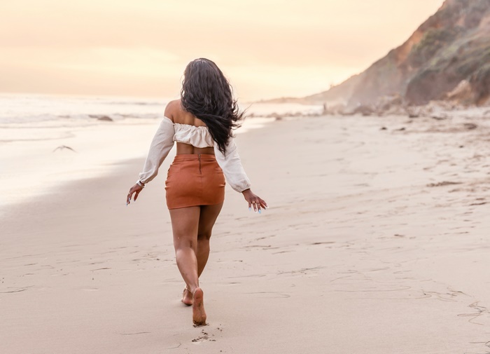 Woman in off-shoulder top and skirt walking on beach