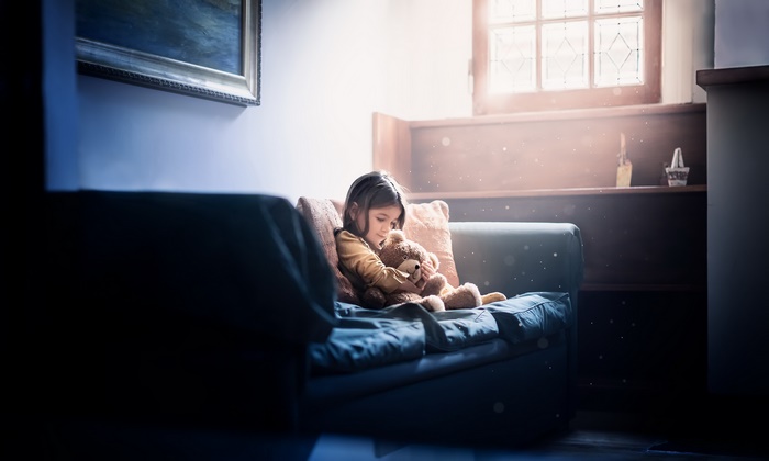 Girl hugging teddy bear on sofa