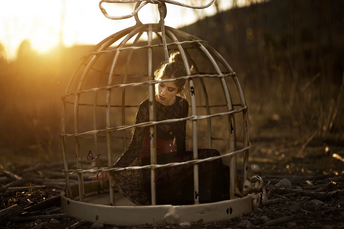 Woman in cage with butterfly at sunset