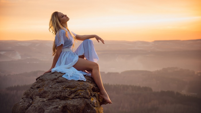 Woman in white dress on rock at sunset