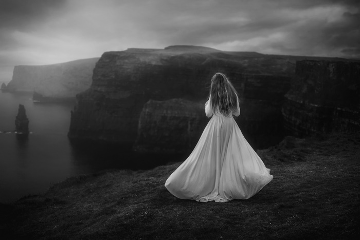 Woman in white dress on cliff overlooking ocean