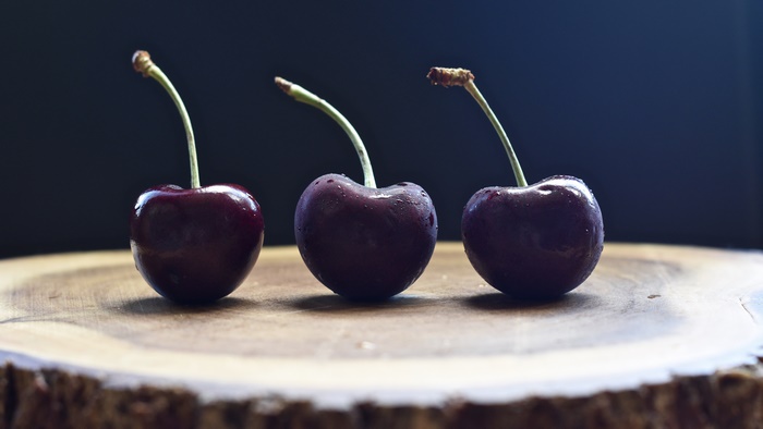 Three cherries with stems on a wooden surface