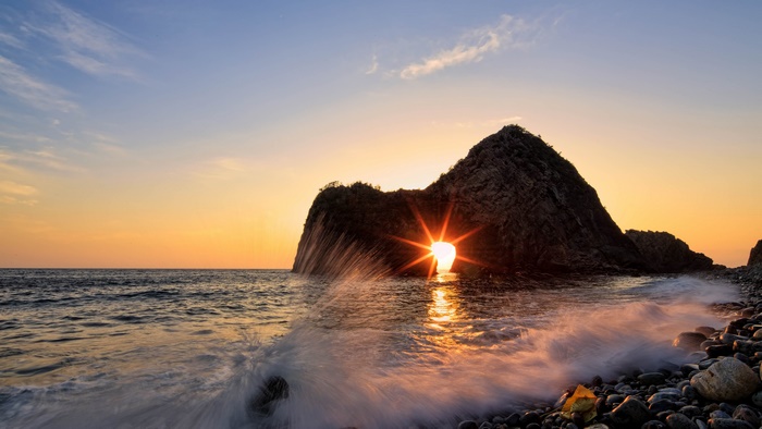 Sunrise through rock arch on a rocky beach
