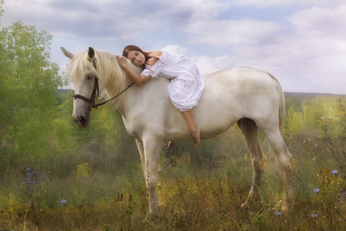 Girl lying on a white horse in a field