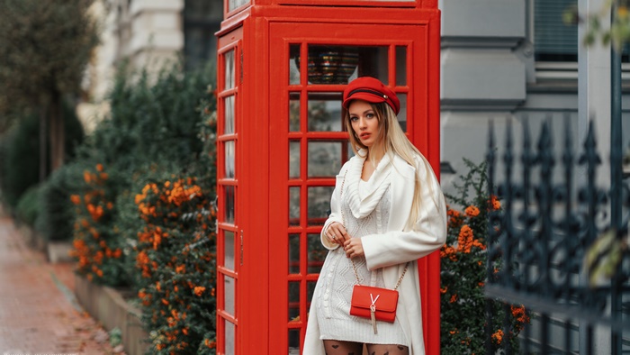 Model in red hat and white coat by red telephone booth