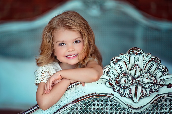 Little blonde girl smiling, leaning on ornate furniture