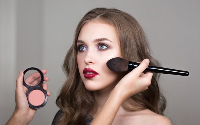 Woman applying blush with makeup brush and blush compact
