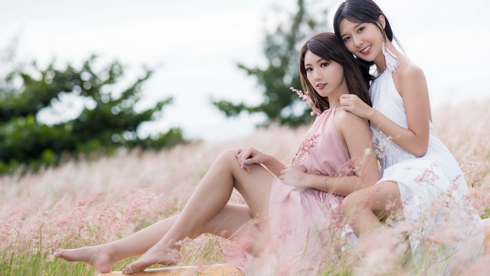 Two Asian women in elegant dresses in a field of flowers