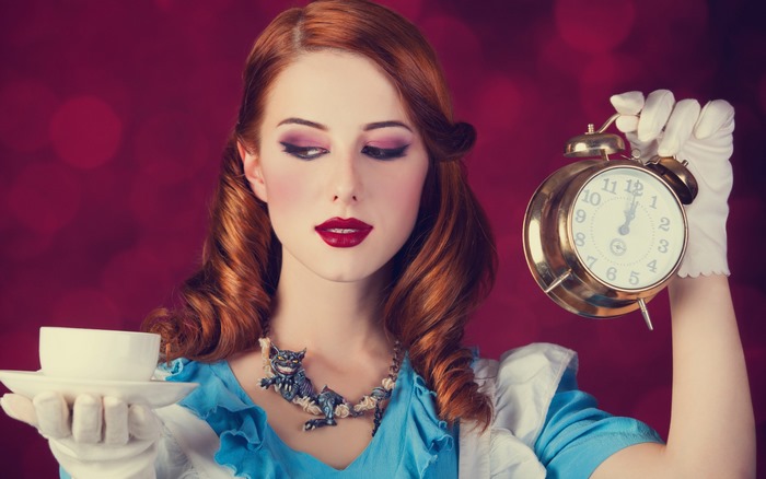 Redhead woman dressed as Alice in Wonderland holding a cup and alarm clock