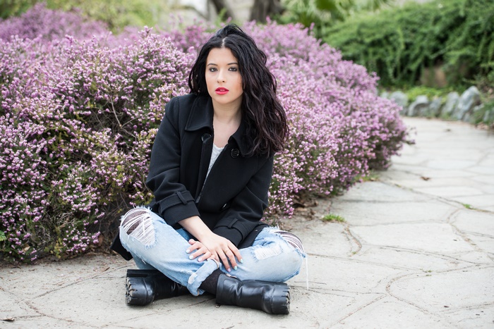 Woman with black hair sitting in front of purple flowers