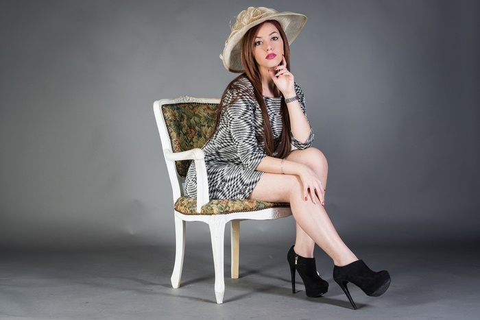 Woman in stylish dress and hat sitting on a chair