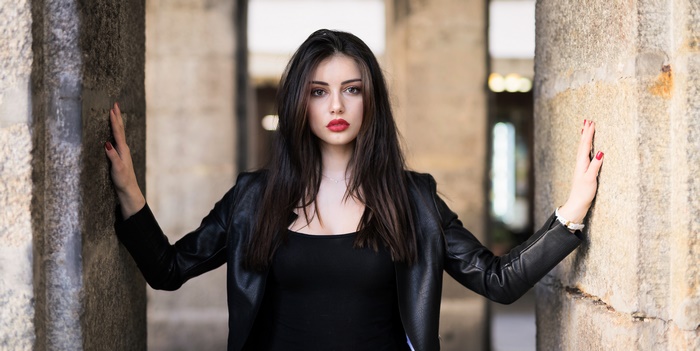 Woman in black leather jacket leaning on stone columns