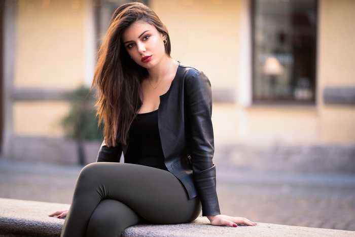 Brunette woman in leather jacket sitting outdoors