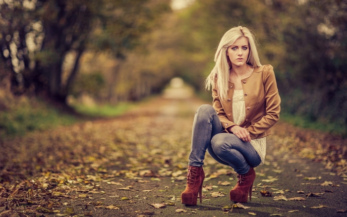 Blonde woman crouching on a leaf-covered path