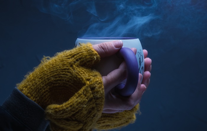 Hands in a yellow knitted glove holding a steaming mug