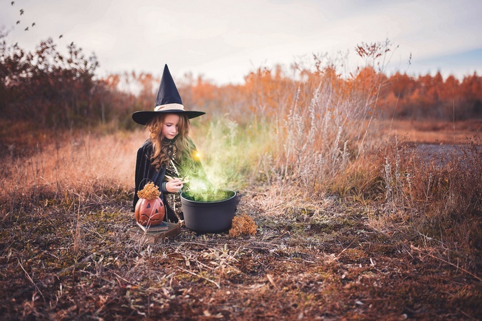 Girl in witch costume making potion in fall field
