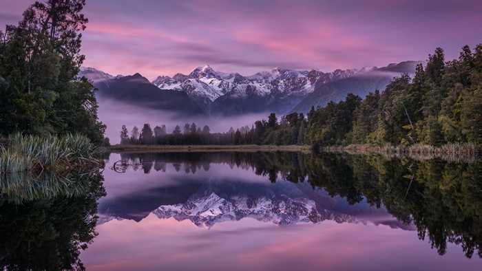 Lake reflection of snow-capped mountains at sunset