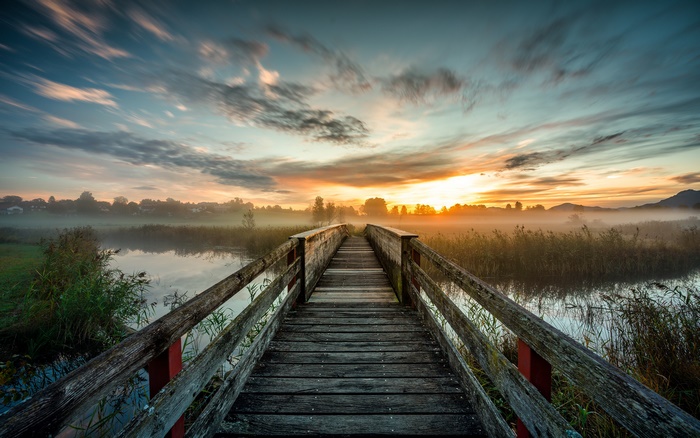 Wooden bridge over a misty lake at sunset