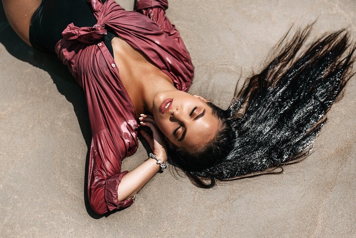 Woman in wet shirt lying on sand