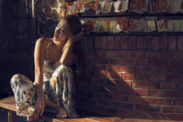 Asian woman in floral dress sitting by brick wall
