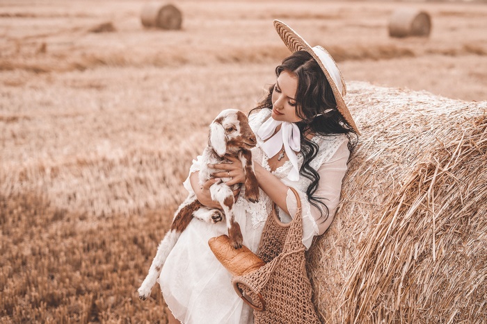Woman in straw hat holding a goat in a hayfield