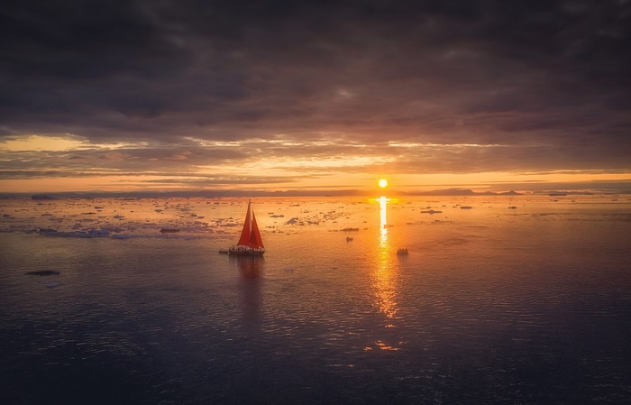 Sailboat with red sail on the ocean at sunset