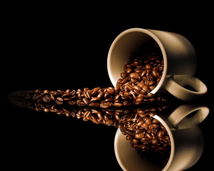Coffee beans spilling from a cup with reflection