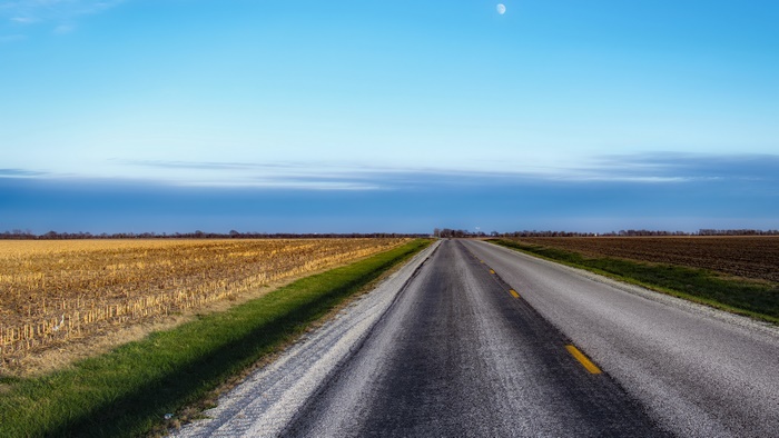 Road through fields under a blue sky with moon