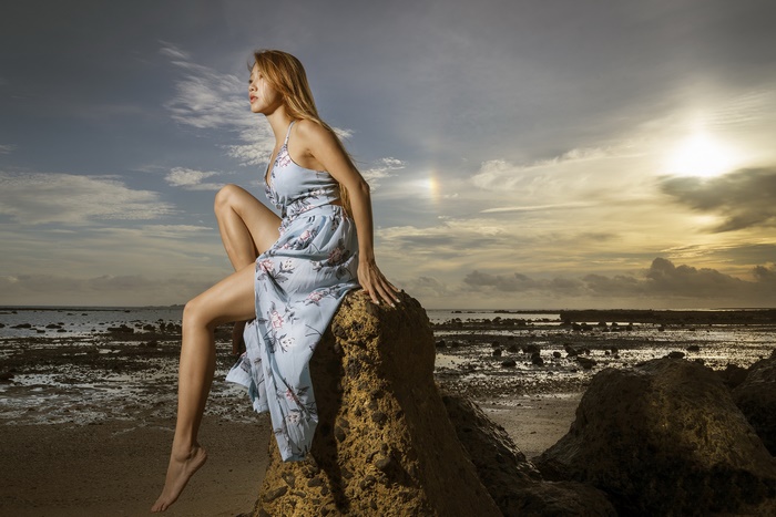 Asian woman sitting on rocks at sunset