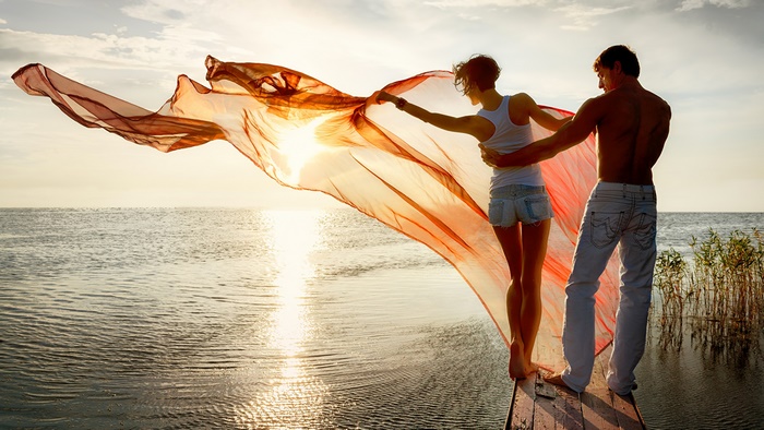 Couple holding fabric by the sea at sunset
