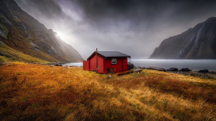 Red cabin on a rocky shore with mountains